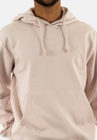 Felpa rosa chiaro realizzata in tessuto morbido, con tasca frontale, cappuccio con cordino e logo in rilievo sul petto.