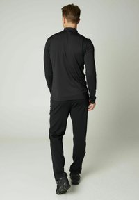 Schwarzes Langarmoberteil und passende Hose, aus einem glatten, dehnbaren Stoff. Das Design zeigt einen hohen Kragen und enganliegende Ärmel.