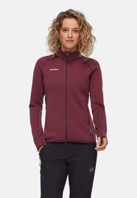 Giacca in fleece bordeaux con colletto alto, tasche con zip e cuciture a contrasto; texture liscia e design aderente per calore e flessibilità.