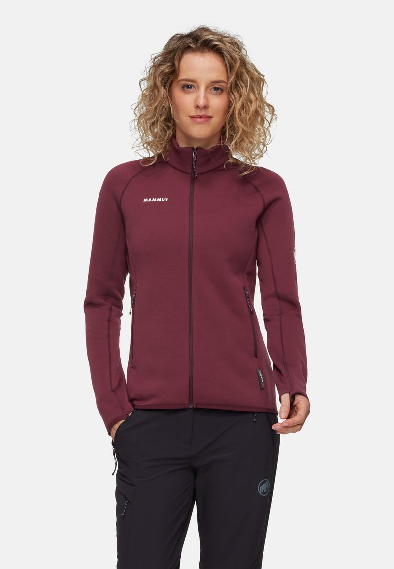 Giacca in fleece bordeaux con colletto alto, tasche con zip e cuciture a contrasto; texture liscia e design aderente per calore e flessibilità.