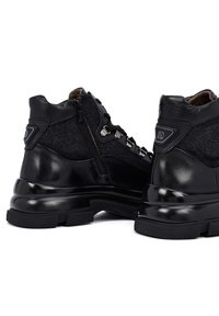 Zapatos negros de caña alta con una combinación de materiales de cuero y textil, con acentos metálicos, un zipper lateral y una suela gruesa y texturizada.