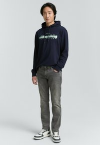 Felpa con cappuccio blu navy con logo "Tom Tailor", abbinata a jeans grigi e sneakers bianche e nere; design casual con una vestibilità comoda.