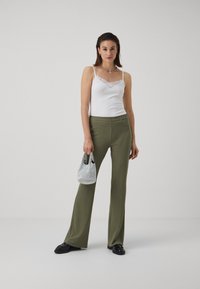 Débardeur blanc avec dentelle, pantalon large côtelé vert olive, mocassins noirs et un petit sac à carreaux gris. Tenue simple et décontractée.