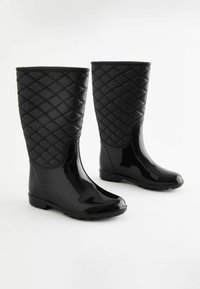 Bottes de pluie en caoutchouc noir avec une tige en texture mat matelassée. Section inférieure brillante et semelle texturée pour une traction. Design montant jusqu'au genou.
