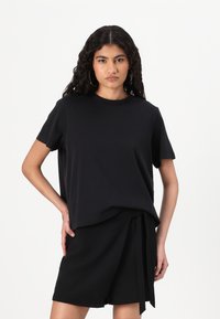Sort t-shirt med korte ærmer lavet af blødt stof med rund halsudskæring, parret med sorte højtaljede shorts med en knyttet detalje.