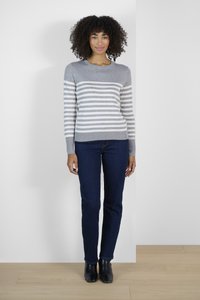 Pull en rayures grises et blanches avec un col rond, associé à un jean droit bleu marine et des bottines noires sur un sol en bois clair.
