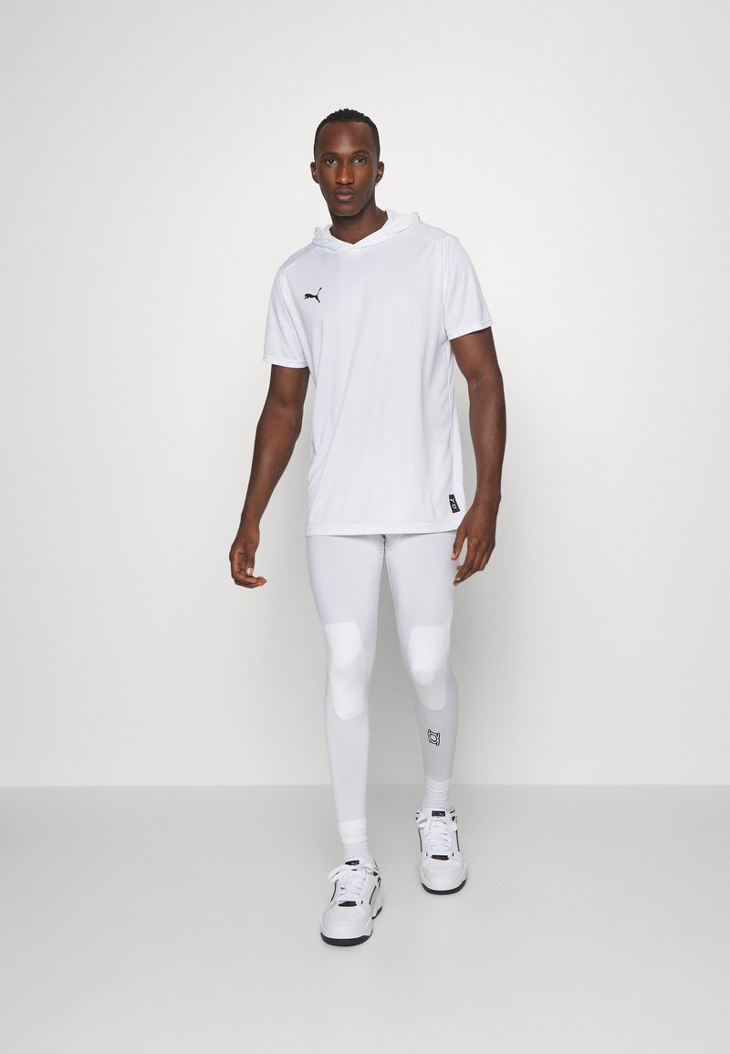 Completo sportivo bianco, composto da una felpa corta a maniche e leggings aderenti. Dettaglio notevole del logo nero sulla parte superiore e imbottitura alle ginocchia dei leggings.