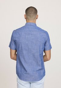 Chemise à manches courtes en tissu bleu clair avec un petit motif blanc. Dotée d'un col classique et d'un ourlet arrondi.