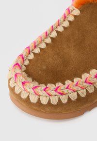 Pantoufle en suède marron avec un bord en fil tressé beige, rose et orange et une semelle en caoutchouc sur fond blanc.