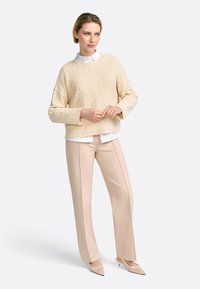 Kreemjat tekstuuri sweater ümmarguse kaelusega, valge kraega särgi kohal. Beezid sirged püksid ja teravad beezid kontsad.