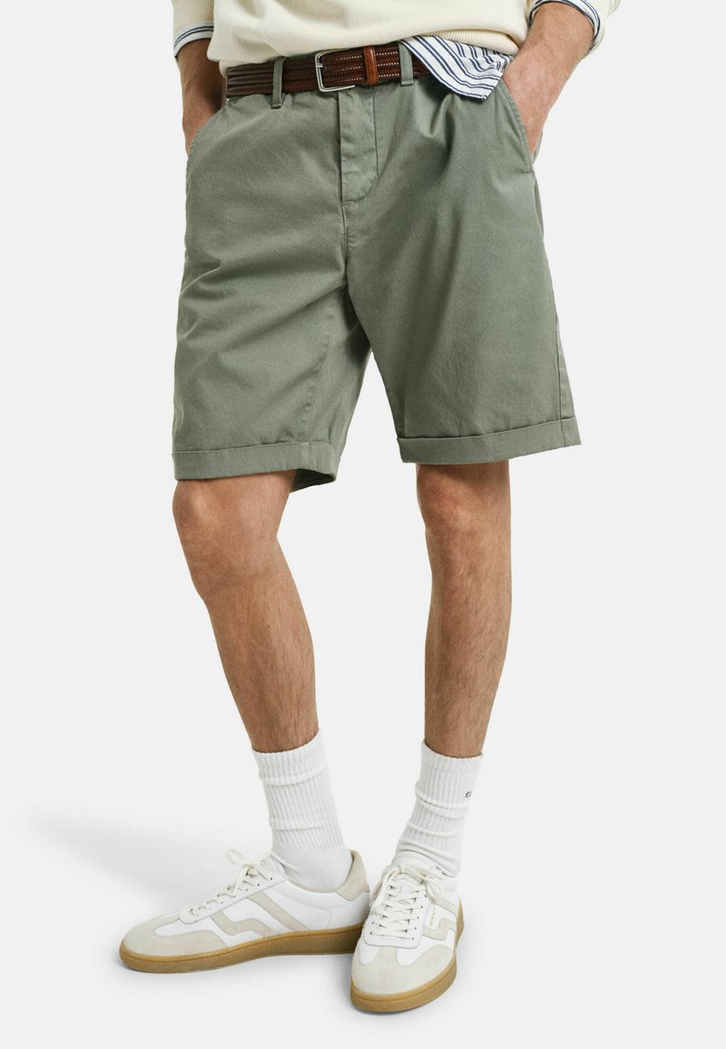 Khakifarbene Baumwollkurzshorts mit umgeschlagenen Säumen, in lockerer Passform, kombiniert mit weißen Sneakers und einem strukturierten braunen Gürtel.