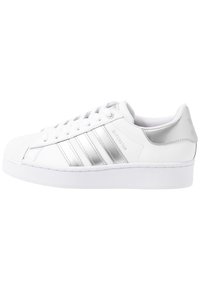 Bílé tenisky Adidas Superstar se stříbrnými pruhy, špičkou ve tvaru mušle, šněrováním a silnou podešví, zobrazené z boku na bílém pozadí.