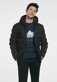 Czarna kurtka puchowa z zamkiem z przodu i kapturem, o gładkiej fakturze. Nosi się ją na granatowej koszulce z grafiką gór. Para ciemnych spodni.