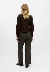 Pull en maille marron à manches longues associé à un pantalon large vert olive. La tenue présente une coupe décontractée et un design minimaliste.