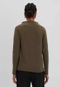 Haut à manches longues vert olive avec un motif texturé, conçu dans une coupe décontractée et avec un col discret, fabriqué en tissu léger.