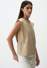 Beżowa bezrękawnik o strukturalnych ramionach, okrągłym dekolcie i bocznych wycięciach. Wykonana z gładkiego materiału o luźnym kroju i estetycznych szwach.