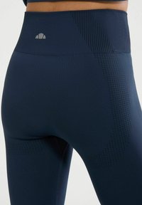 Granatowe legginsy o wysokim stanie z teksturowanymi akcentami i perforowanymi wzorami po bokach dla lepszej oddychalności. Dyskretny detal z logo na pasku.