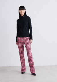 Chemise noire à manches longues avec col montant, associée à un pantalon à carreaux roses avec des accents noir et blanc, portée avec des talons noirs pointus.