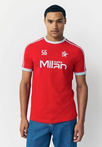 Czerwona krótki rękaw sportowa koszulka z niebieskimi akcentami. Zawiera logo "Milan" i numer "56" w białym tekście. Gładki materiał, okrągły dekolt.