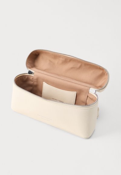 Κρεμ ορθογώνια θήκη με φερμουάρ, ανοιχτή αποκαλύπτοντας εσωτερικό από ταμπά ύφασμα και μια μικρή ραμμένη τσέπη στο εσωτερικό.