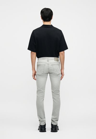 Μαύρο πόλο μπλουζάκι, ανοιχτό γκρι τζιν και μαύρα παπούτσια, σε θέα από πίσω. Το τζιν έχει πίσω τσέπες και διακοσμητική υφή στη ζώνη της μέσης.