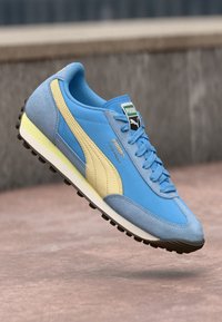 Tenis em camurça azul e amarelo com um cabedal texturizado, fecho de atacadores e uma sola de borracha preta, apresentando uma etiqueta de logo na língua.