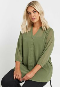 Blusa leggera verde oliva con scollo a V, chiusura a bottoni e maniche 3/4 trasparenti. Texture liscia con vestibilità rilassata.