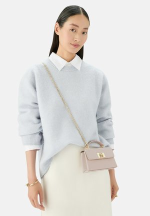 Lichtblauw sweater gemaakt van zachte stof, met een geribbelde halslijn. Houdt een kleine roze handtas met gouden hardware vast, gedragen over een witte rok.