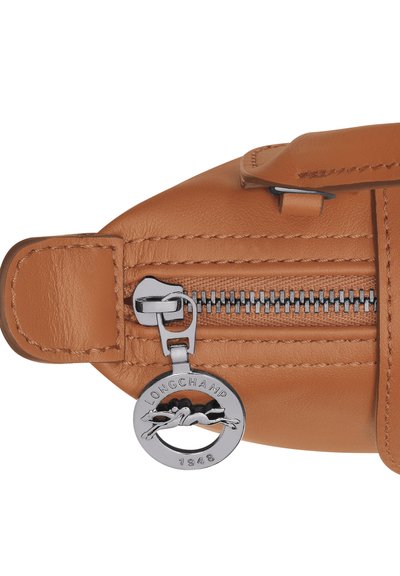 Braune Ledertasche mit einem Metallreißverschluss und einem silbernen Anhänger. Der Anhänger zeigt "LONGCHAMP 1948" und ein Logo eines galoppierenden Pferdes.