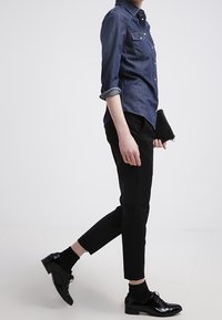 Denimskjorta med knappad krage, två bröstfickor; svarta ankelbyxor; blanka svarta dressskor; svarta strumpor.