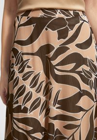 Jupe évasée en tissu léger présentant un motif de feuilles marron et beige avec des contours blancs. Texture lisse, taille mi-haute.
