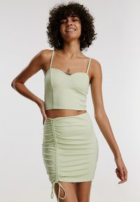 Lichtgroene crop top met een sweetheart-halslijn, dunne bandjes en een bijpassende gerimpelde minirok met strikdetails aan één kant.