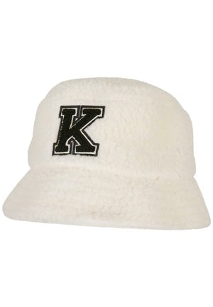 Hvid, fuzzy bøttehat lavet af tekstureret stof med et sort broderet bogstav "K" foran. Flad skygge og rundt krone-design.