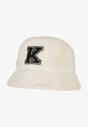 Valge, karvane ämbri müts, mis on valmistatud tekstuurnahast, musta tikkimisega tähega "K" esiküljel. Lame ääre ja ümar kroonideisain.