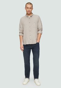 Lichtgrijze button-up shirt met lange mouwen, borstzak, gecombineerd met donkerblauwe jeans en witte sneakers. Eenvoudig, casual ontwerp.