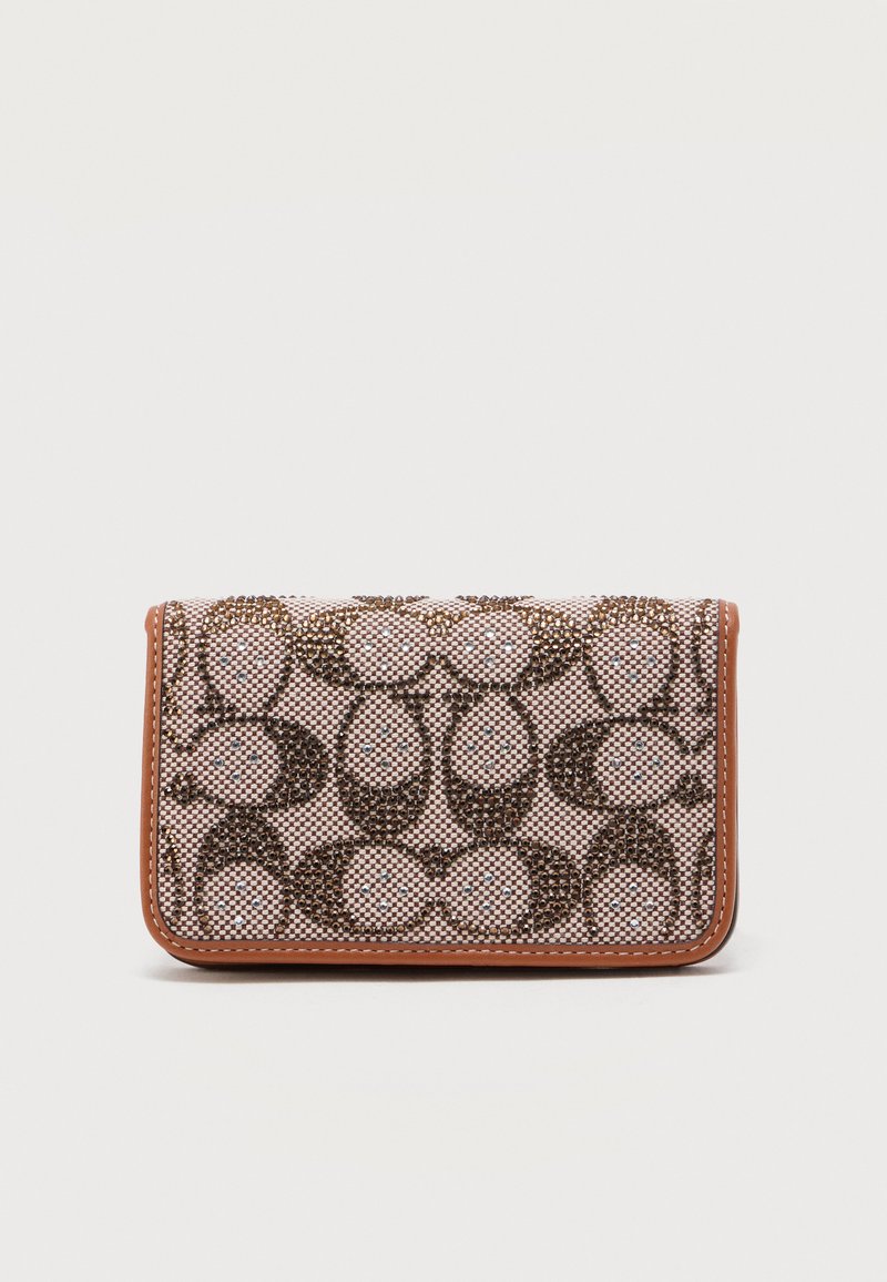 Ορθογώνιο μπεζ πορτοφόλι με καφέ μοτίβο μονόγραμμα, διακοσμητικά καρφιά και καφέ δερμάτινη επένδυση στις άκρες, κλειστό και όρθιο σε λευκή επιφάνεια.