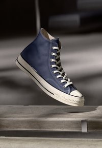 Helle High-Top-Sneaker aus dunkelblauem Leder mit weißen Schnürsenkeln, kontrastierender Gummisohle und Zehenschutz. Verfügt über eine strukturierte Oberfläche und Seitensteppnähte.