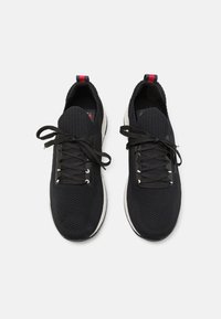 Schwarze Sportschuhe mit strukturiertem Obermaterial, ausgestattet mit schwarzen Schnürsenkeln und einer weißen Zwischensohle, akzentuiert durch eine rote und blaue Lasche an der Ferse.