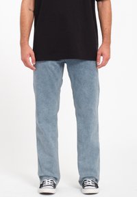 Light blue denim jeans with a straight fit, featuring a faded texture. Paired with a black t-shirt and black sneakers.