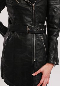 Giubbotto in pelle nera con design aderente, tasche con zip e cintura in vita arricciata con una fibbia in metallo argentato e occhielli.