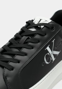 Zwarte leren sneaker met zwarte veters, witte zool en Calvin Klein Jeans-logo op de zijkant en de tong.
