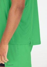 Groene sportshirt met een textuurpatroon, korte mouwen en een zijsplit, gecombineerd met bijpassende shorts waarop het woord "ENDURANCE" is gedrukt.
