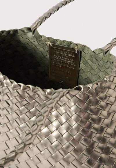 Metallisk vävd toteväska med olivgrön foder. Har flätade handtag och en metalldekal med skötselanvisningar inuti.