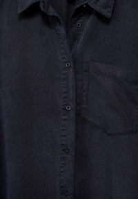 Tmavě modrá košile na knoflíky s límečkem, jednou náprsní kapsou a hladkým texturovaným materiálem. Obsahuje odpovídající knoflíky po přední straně.