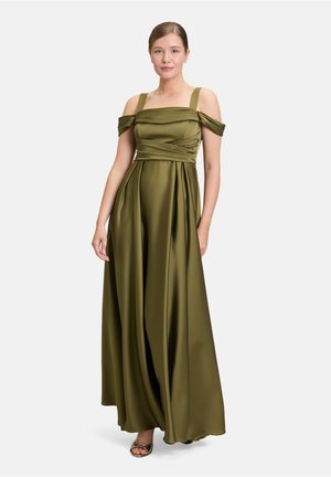 Olijfgroene satijnen avondjurk met off-shoulder mouwen, geplooide lijf en vloeiende rok. Metallic sandaaltjes met straps zijn zichtbaar onderaan.