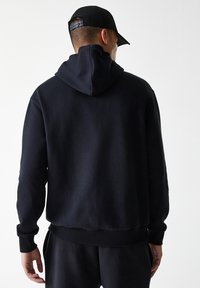 Sudadera de algodón negra con una gran capucha, puños acanalados y dobladillo. Textura suave y corte relajado, con un diseño limpio y minimalista.