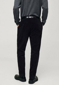 Čierne kordové nohavice so slim fit strihom, s zadnými vreckami a hladkým čiernym opaskom. Textúra je ribbovaná s jemným povrchom.