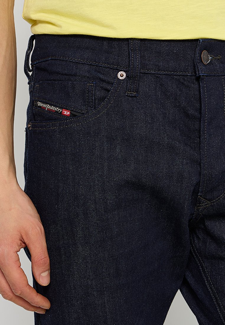 Jeans in denim blu scuro con una vestibilità slim, dotati di un piccolo tag logo rosso e bianco, bottone e rivetti in rame, e design classico a cinque tasche.