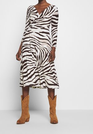Vrouw draagt een lange mouw, zwart-wit zebra gestreepte midi-jurk gecombineerd met beige suède cowboylaarzen halverwege de kuit.