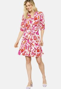 Kukallinen mekko, jossa on vaaleanpunaisia ja oransseja kuvioita, lyhyet puffihihat, kauluspääntie, vyötäröltä kireä ja liehukasa skirt.